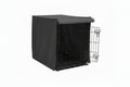 Dog sitting next to a black dog crate with a cover on a white background